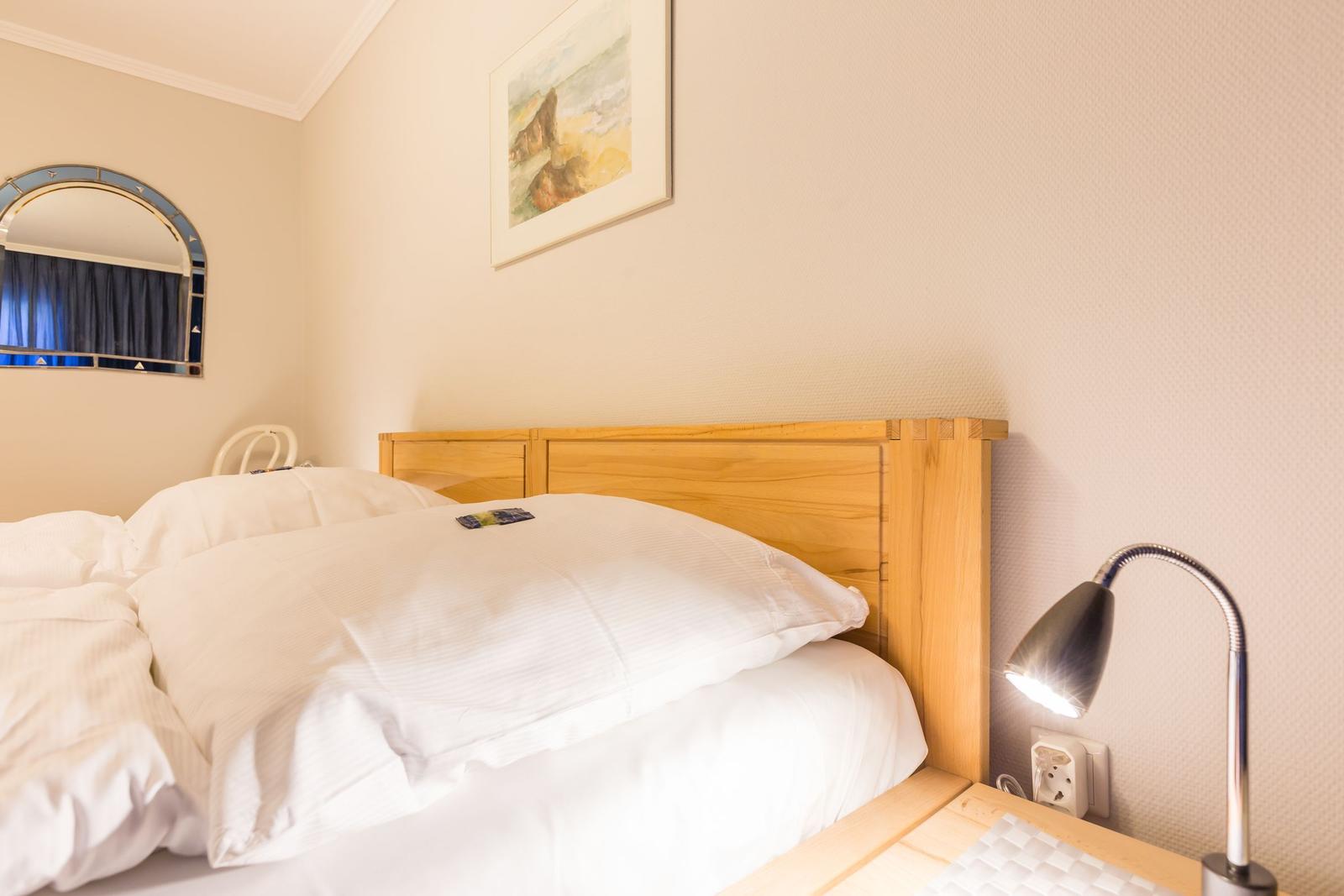 Ein Bett mit weißer Bettwäsche, Holzkopfteil, Stehlampe und Wandbild.