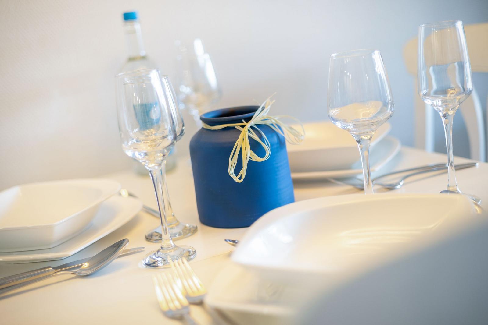 Tisch mit weißen Tellern, Gläsern und blauem Vasenobjekt.