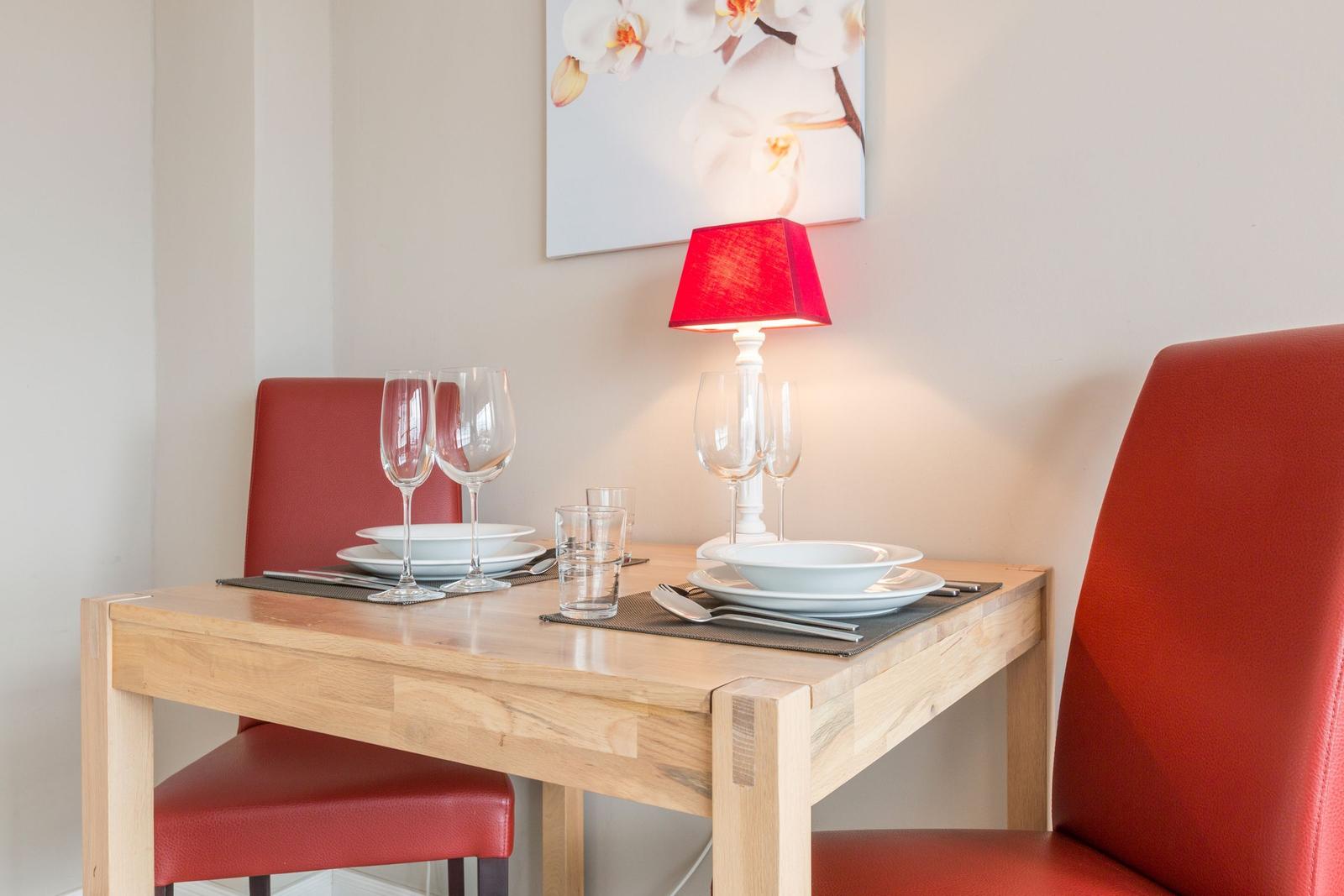 Wooden table with two red chairs, placemats, glasses, and a red lamp.
