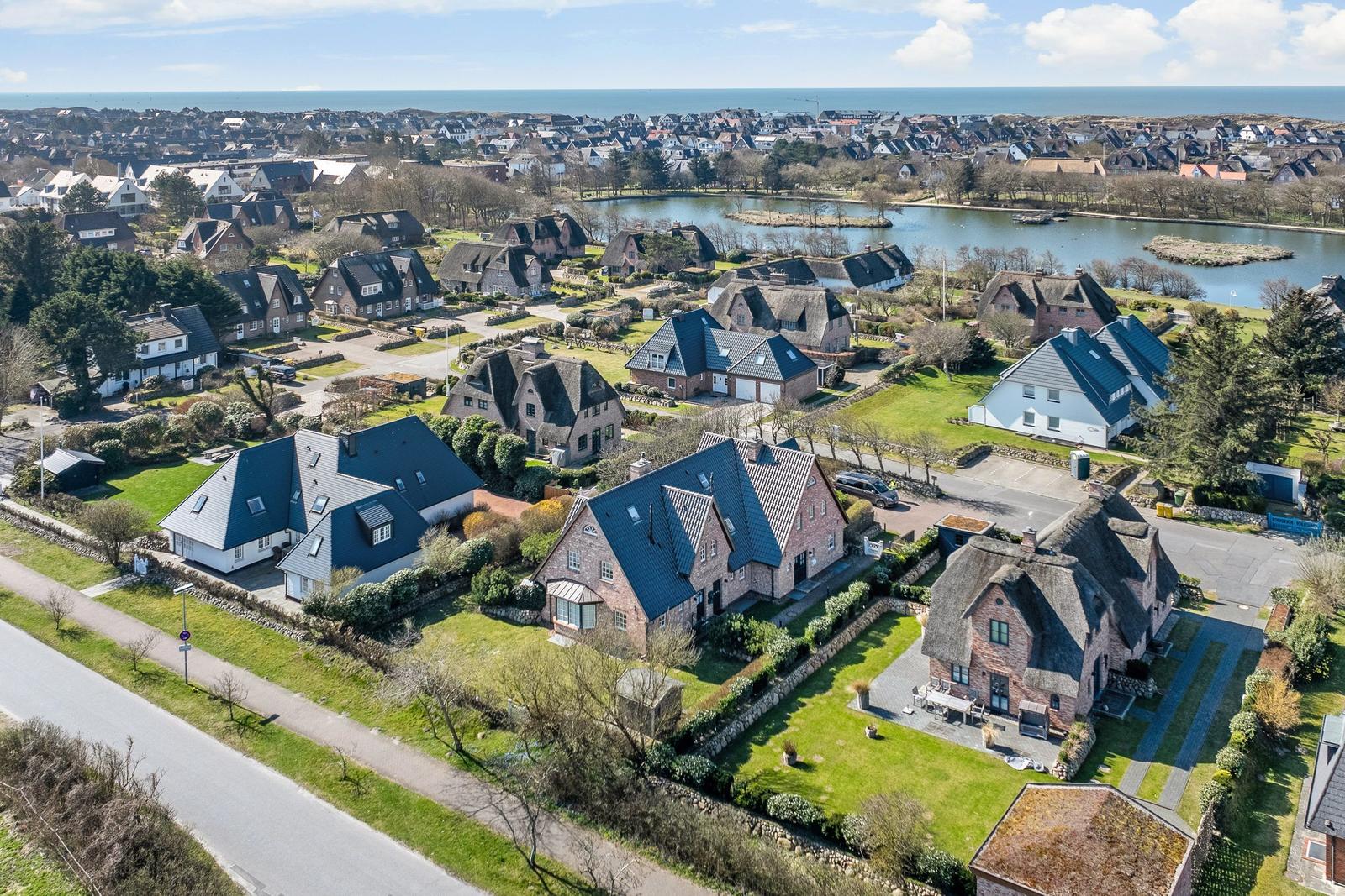 Aerial view of a coastal village with houses, green lawns, and a lake near the sea.