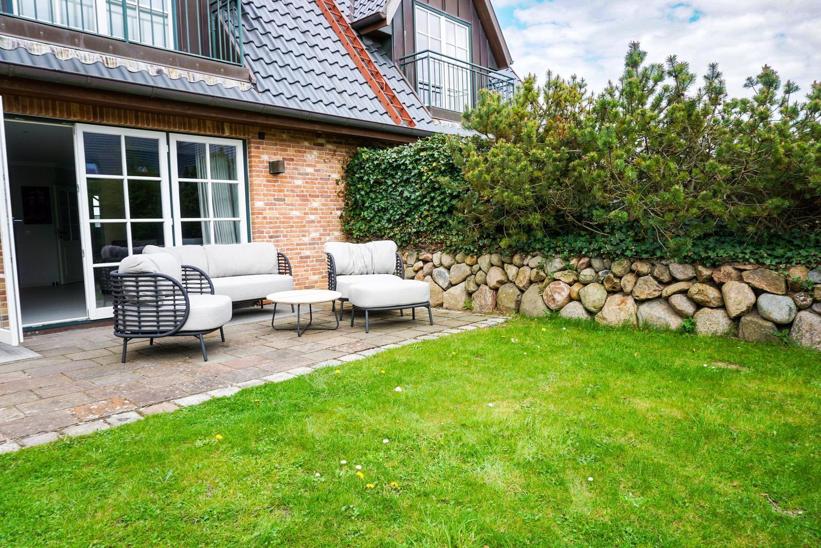 Terrace with seating area and garden. House with stone wall and green hedge.