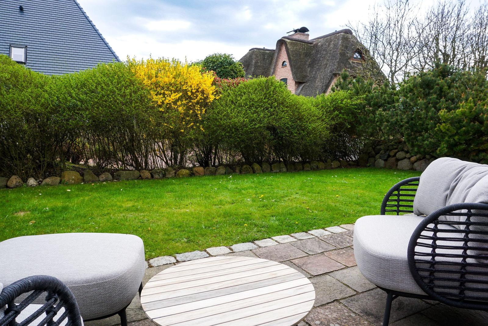 Terrace with seating and view of a lawn and hedges.