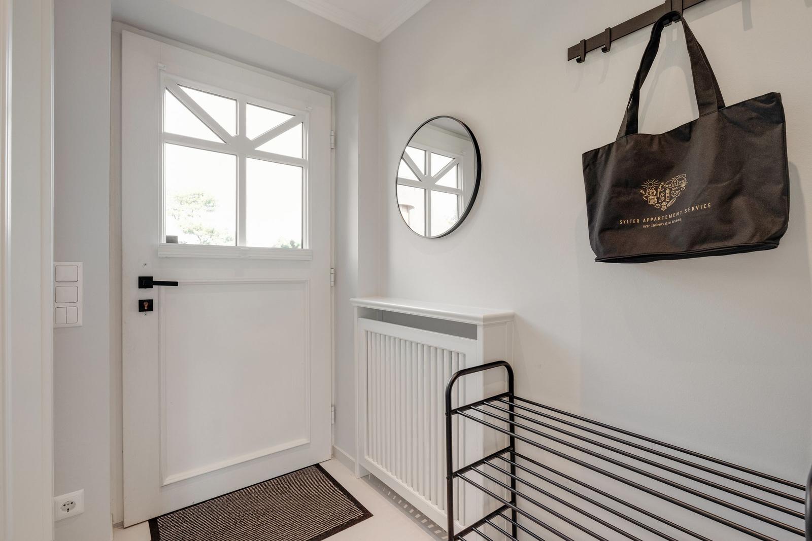 Entrance with white door, round mirror, and hooks for bags.