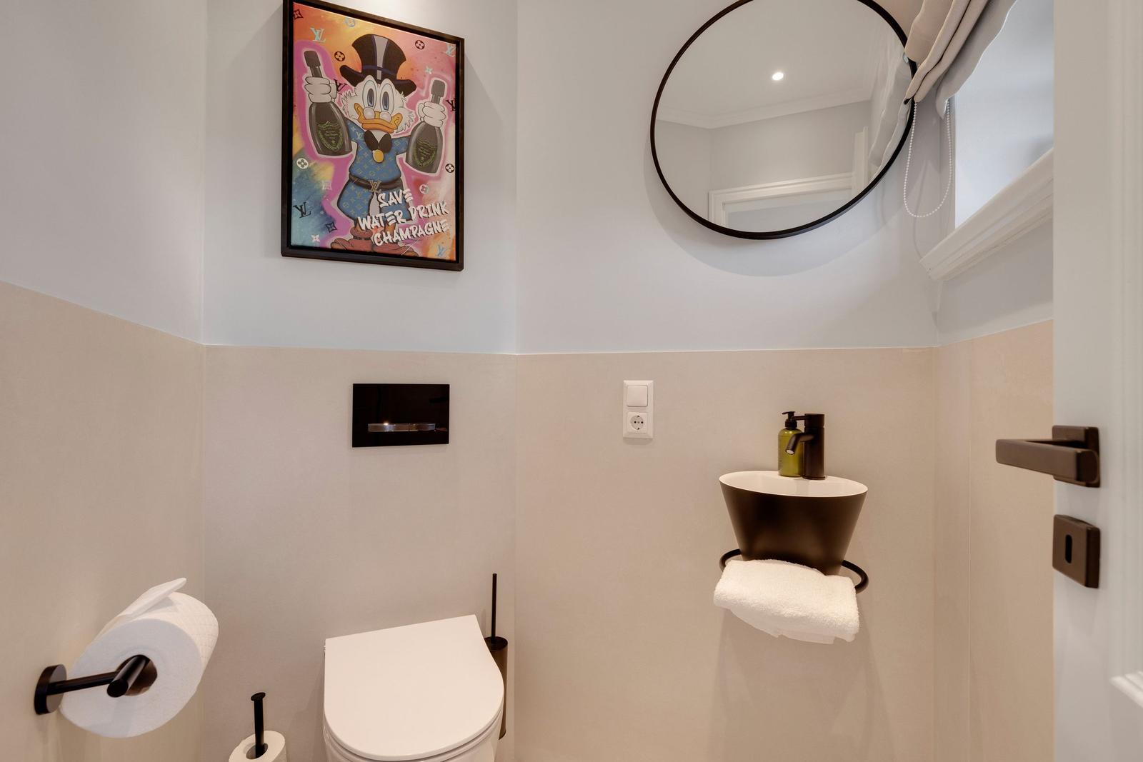 Bathroom with toilet, sink, and wall mirror. Wall art and towel holder visible.