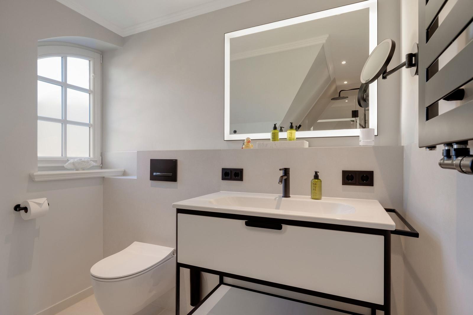 Bathroom with sink, mirror, and toilet. Window and modern fixtures.