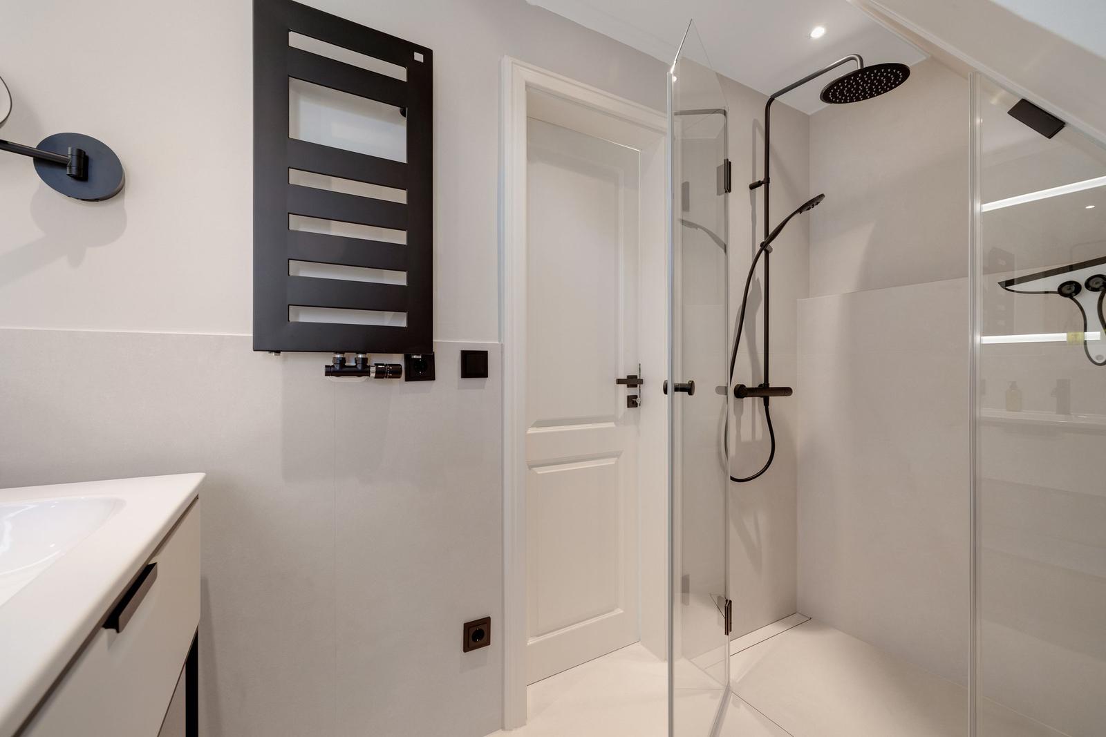Modern shower with glass enclosure and black fixtures. White walls and sink.