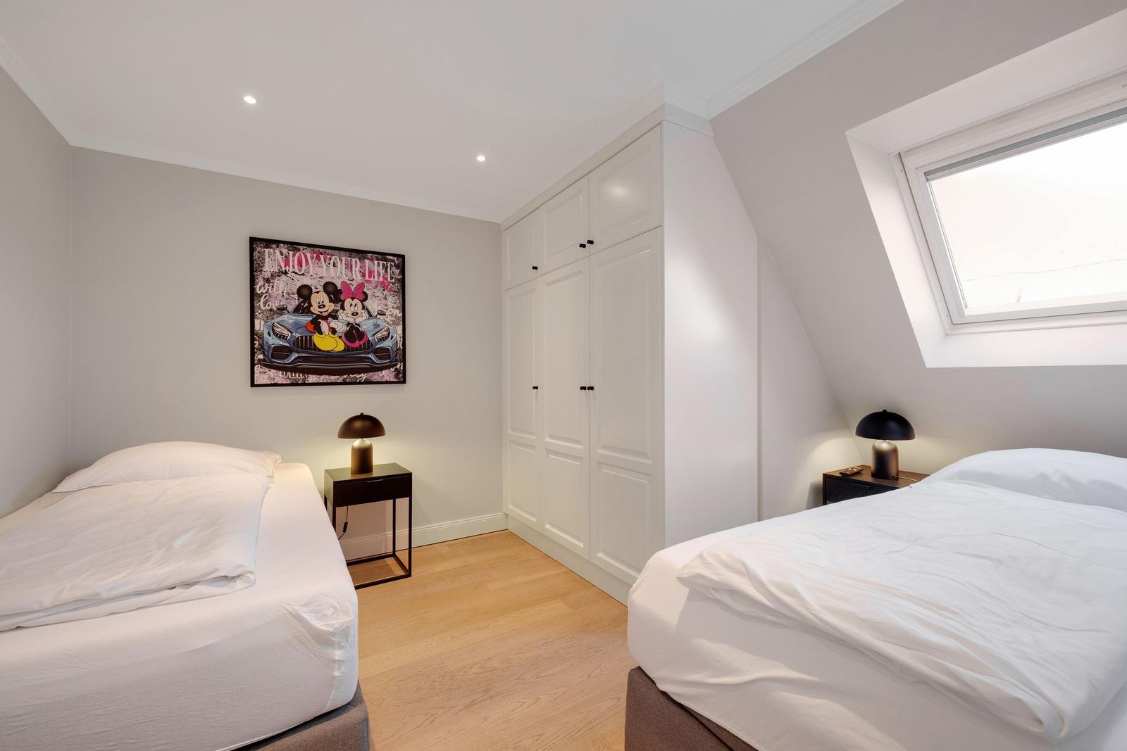 Two beds, wardrobe, and window in a bedroom.