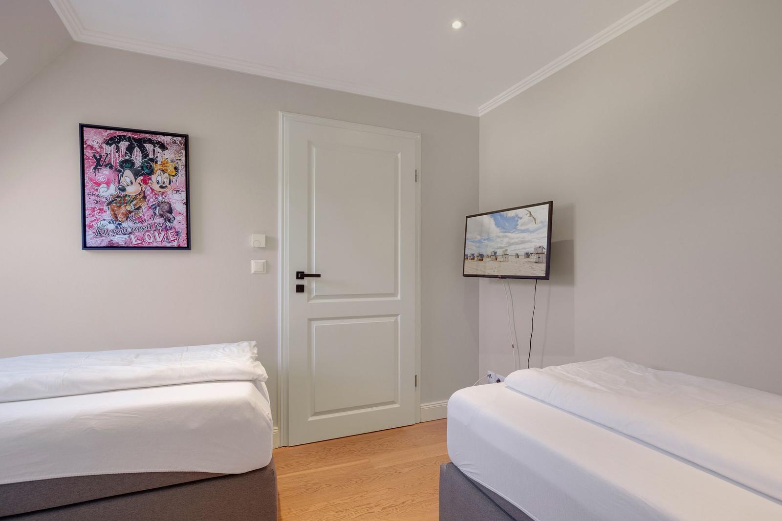 Two beds, wall art, and TV in a bedroom.