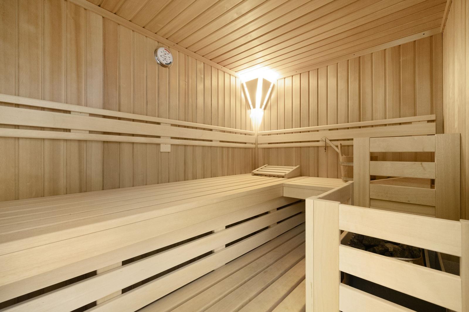 Sauna with wooden bench, stove, and thermometer on the wall.