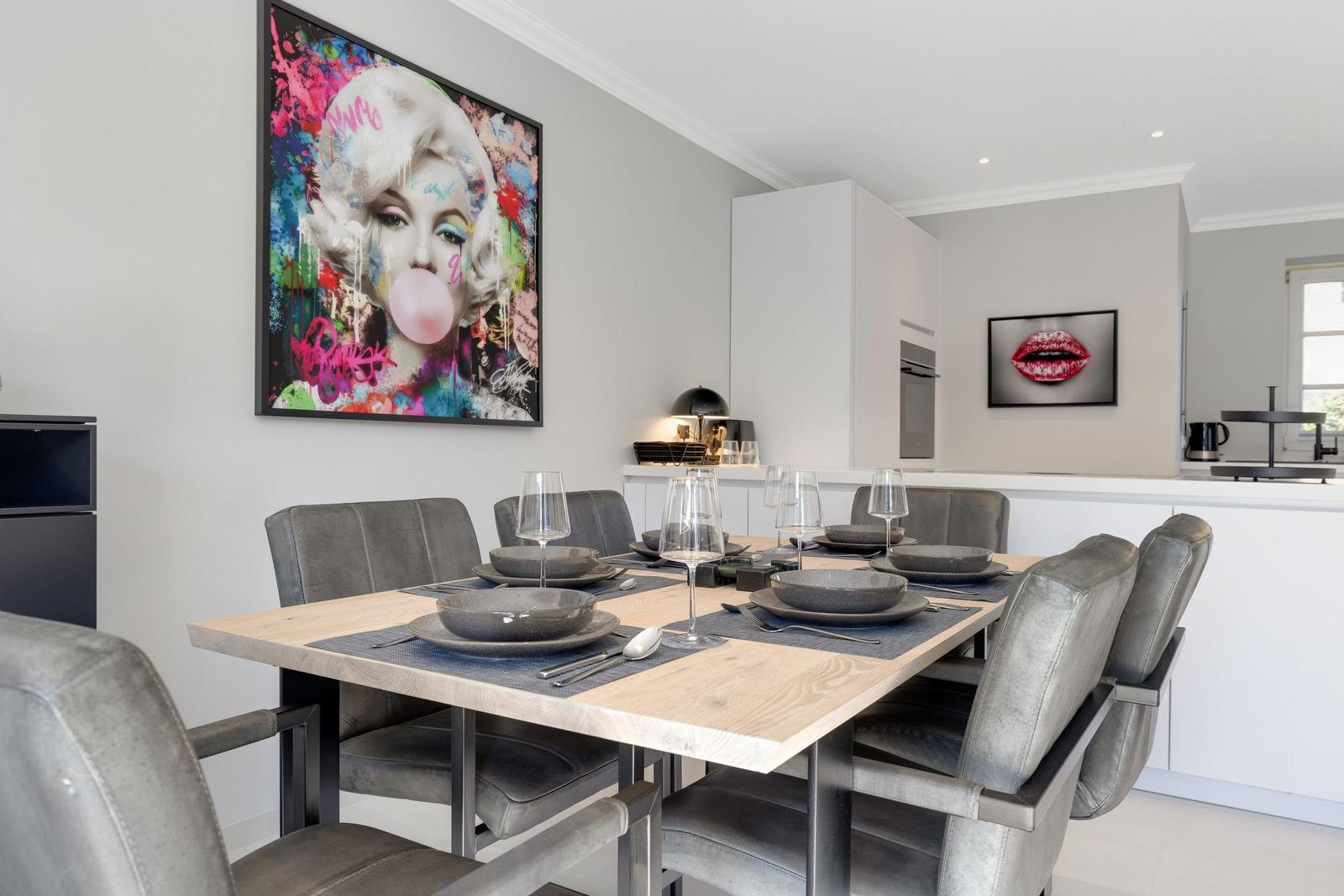 Dining table with chairs, wall art, and kitchen area.