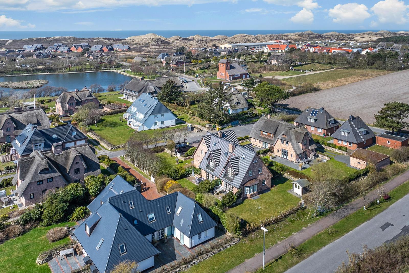 Aerial view of houses with green areas and sea view.
