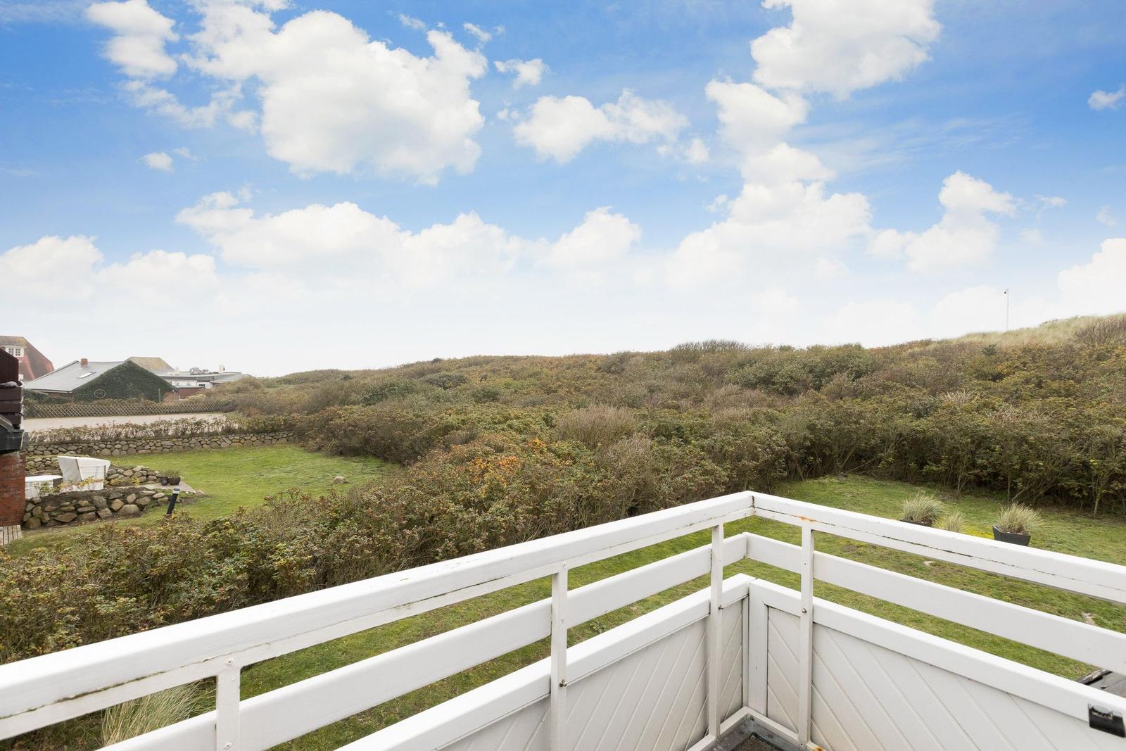 White balcony with view of green meadows and hills under blue sky with white clouds.