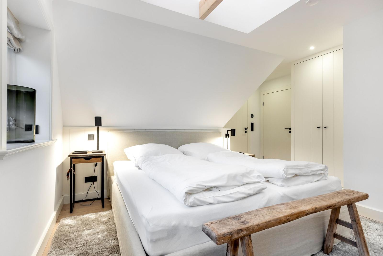 Schlafzimmer mit Doppelbett, Holzbank und Nachttisch unter Dachschrägen.