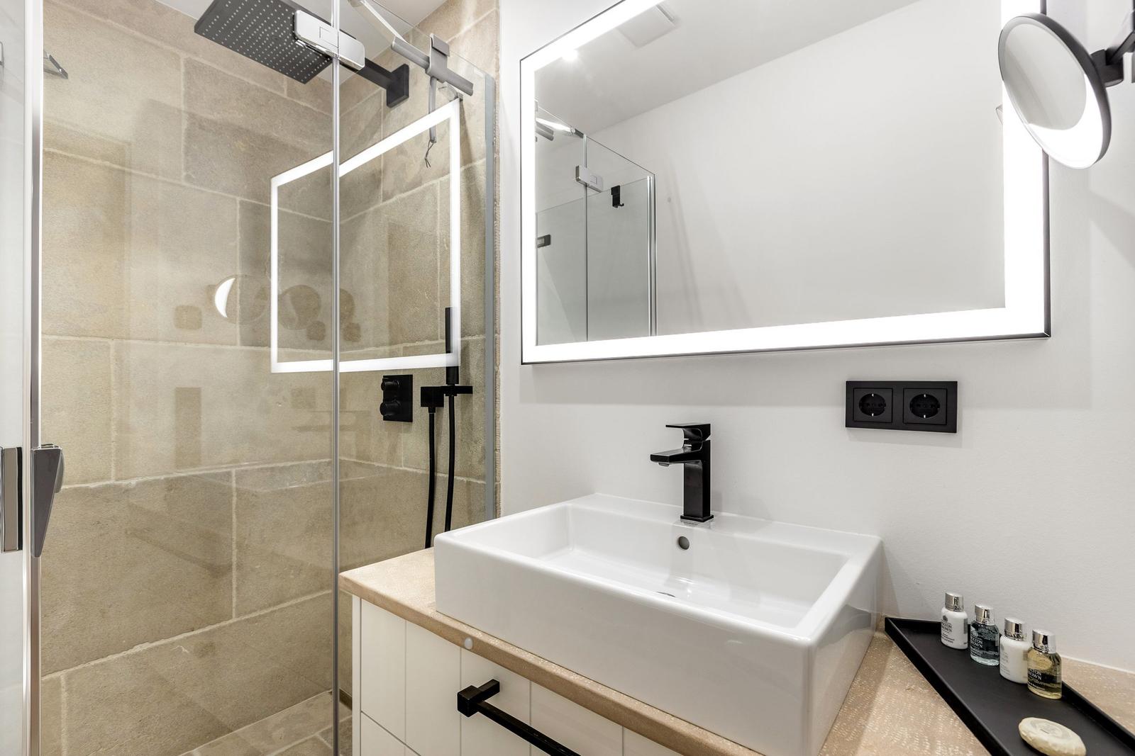 Badezimmer mit Dusche, Waschbecken und beleuchtetem Spiegel