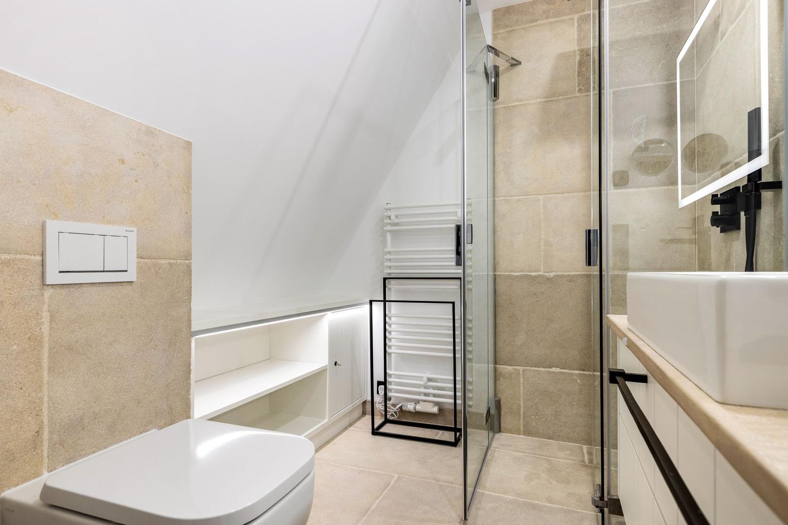 Badezimmer mit Dusche, Waschbecken und Toilette unter Dachschrägen.