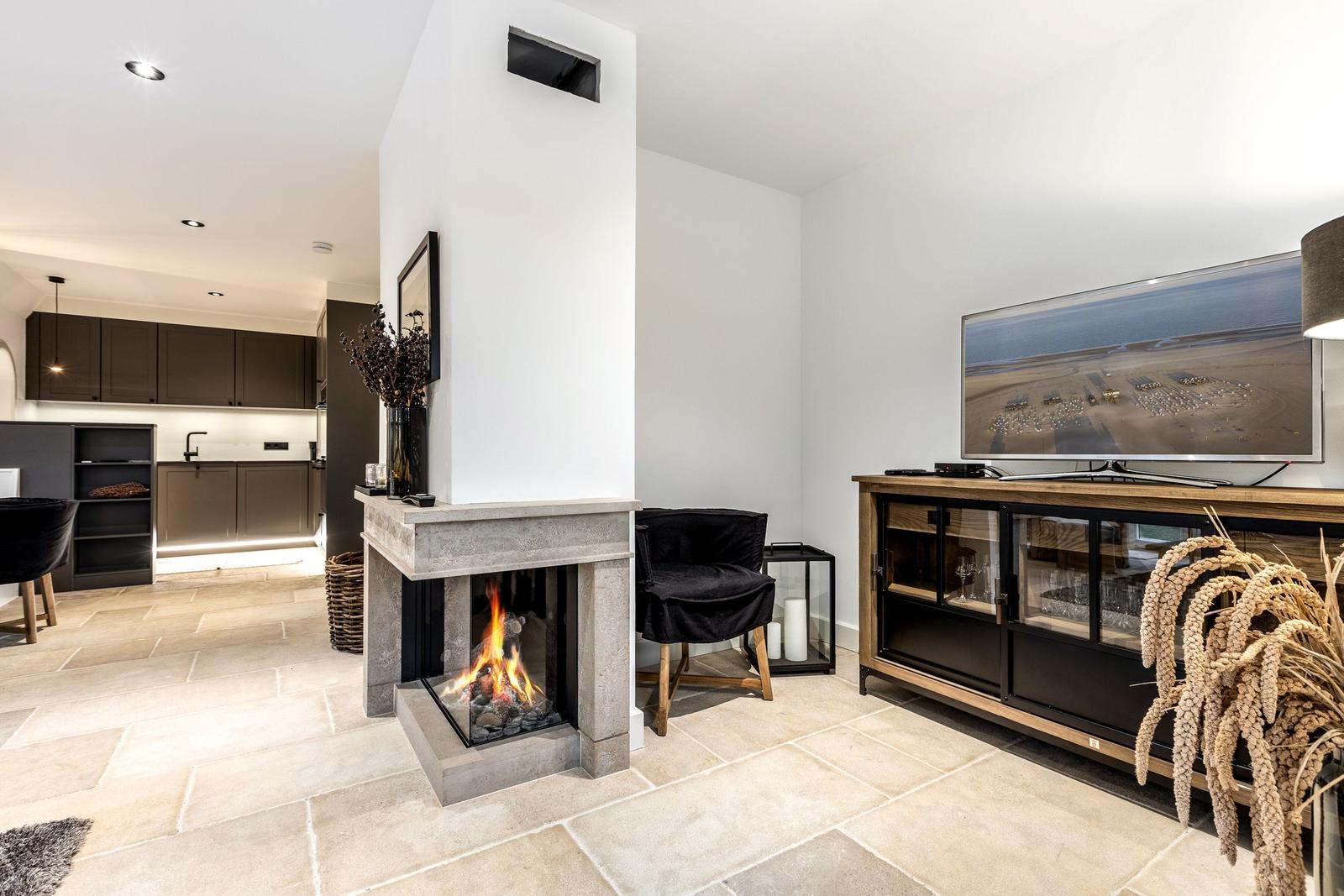 Wohnbereich mit Kamin, Fernseher und Küchenbereich im Hintergrund.