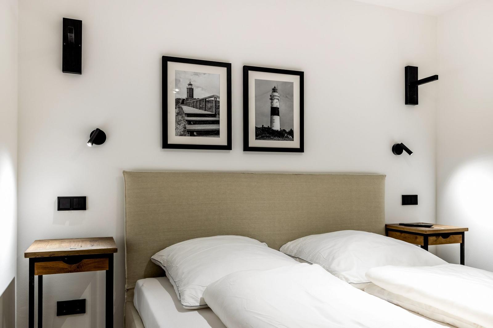 Schlafzimmer mit Bett, zwei Nachttischen und zwei Wandbildern von Leuchttürmen.