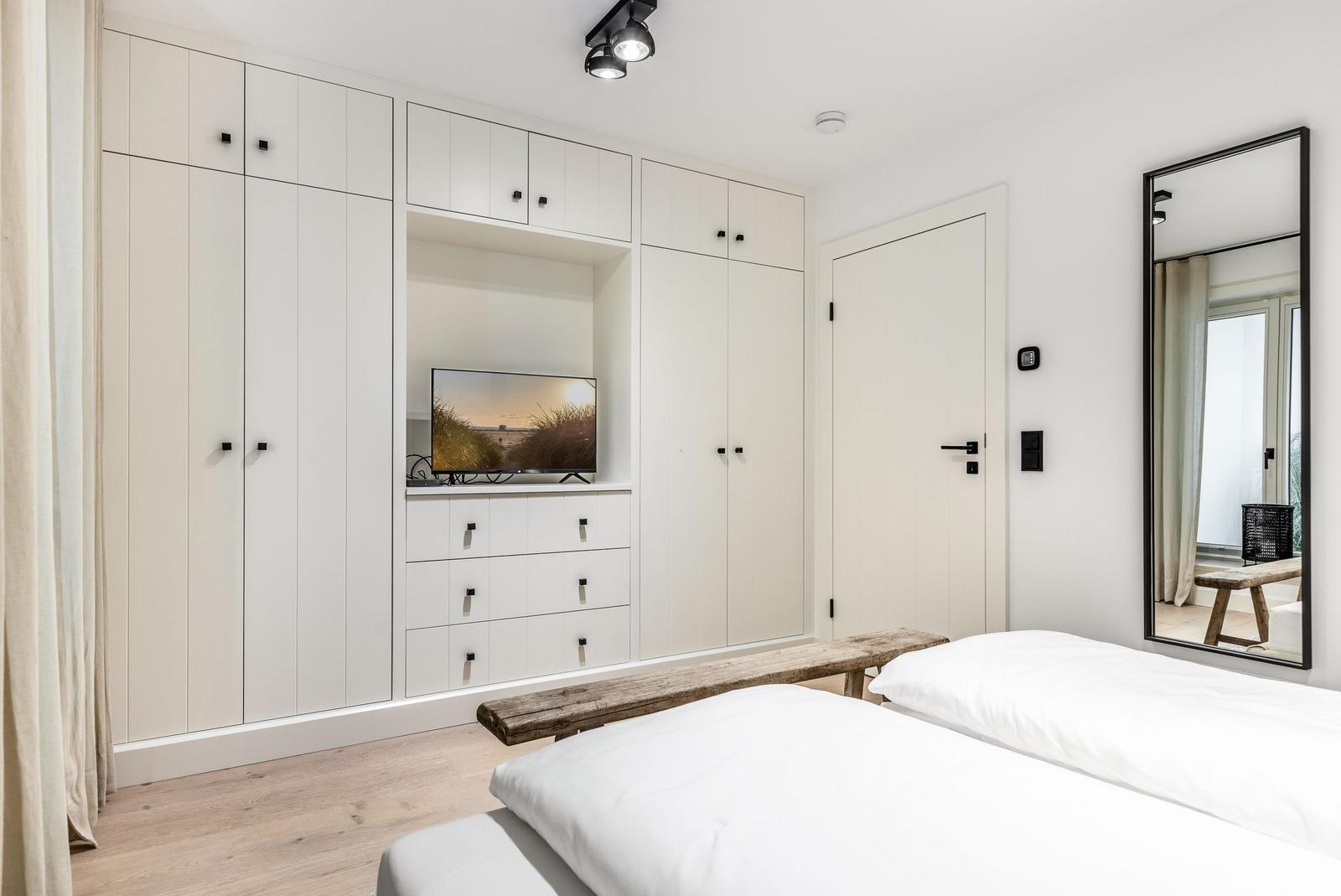 Schlafzimmer mit weißem Schrank, Fernseher und Spiegel.