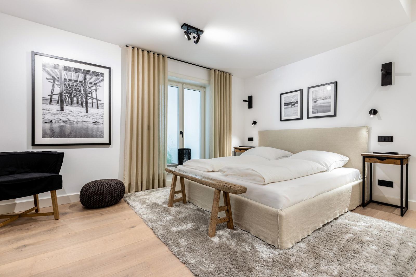 Schlafzimmer mit Bett, Fenster, Wandbildern und Holzboden.