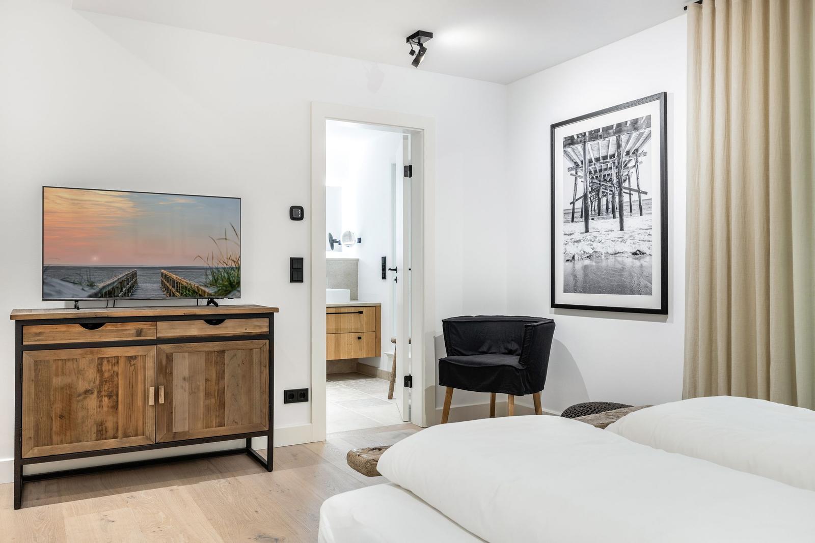 Schlafzimmer mit TV, Stuhl und Blick in Badezimmer