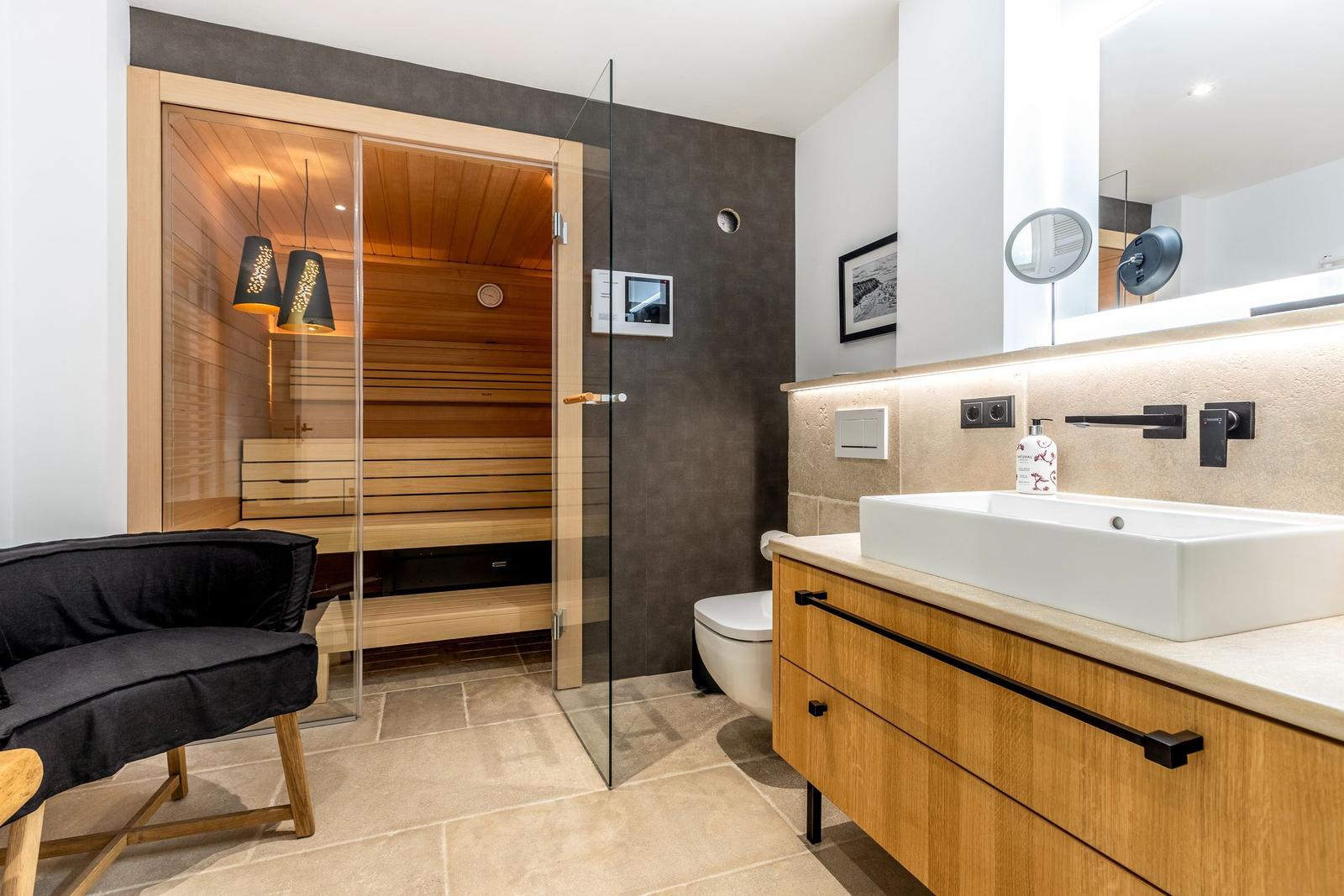 Bad mit Sauna, Waschbecken und Toilette. Glaswand trennt Sauna vom Rest.