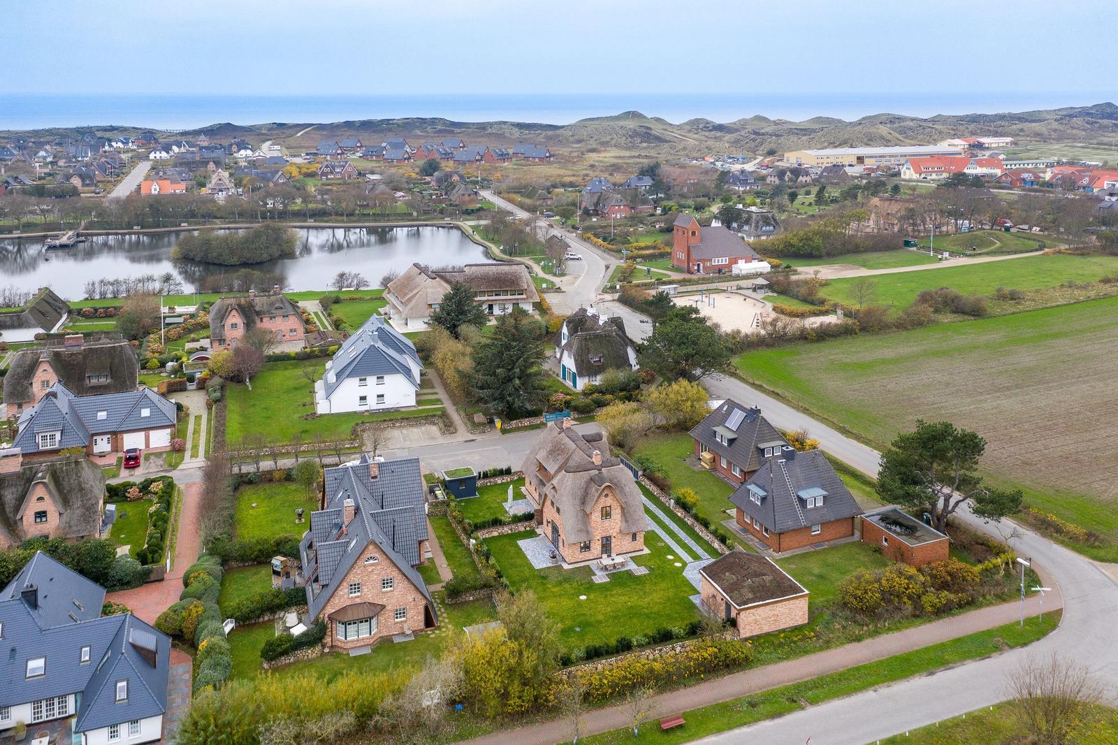Dorf mit Häusern, Teich und Hügeln in der Ferne