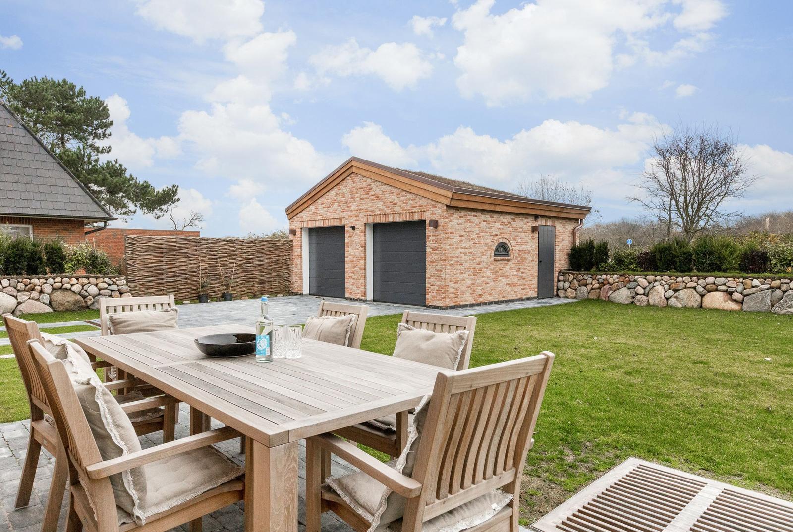 Hinterhof mit Holztisch, Stühlen und Grill. Im Hintergrund steht ein Backsteinhaus mit Garage.