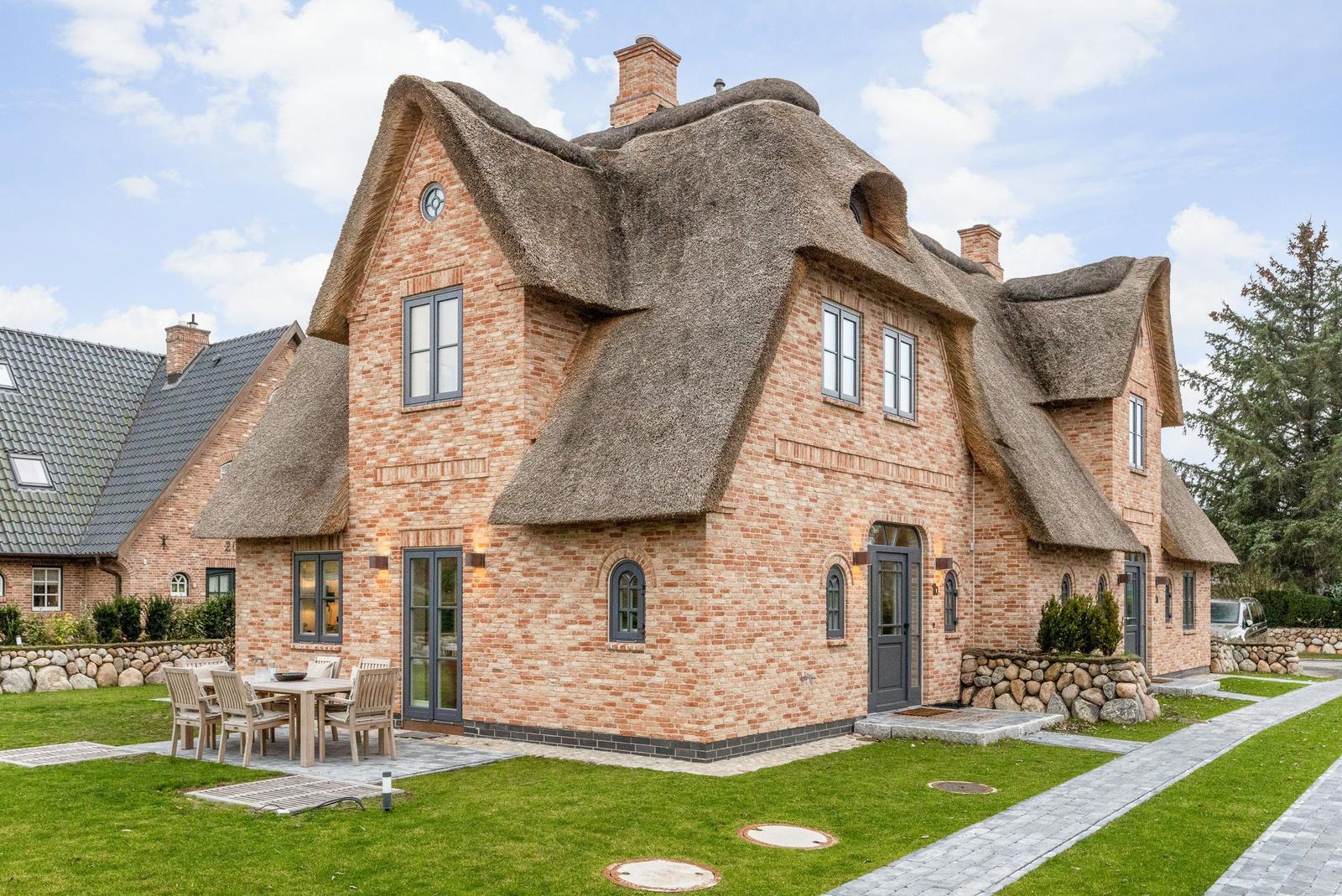 Haus mit strohgedecktem Dach und Steinmauer. Außenterrasse mit Tisch und Stühlen.