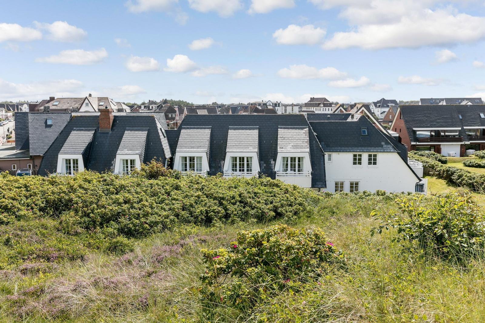 House with dark roof and white windows on a green hillside.