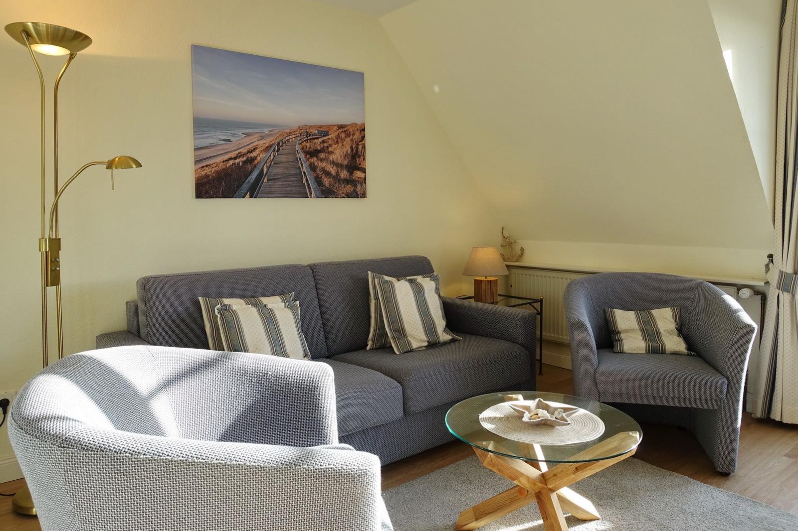 Living room with sofa, armchairs, and glass table under sloped ceiling