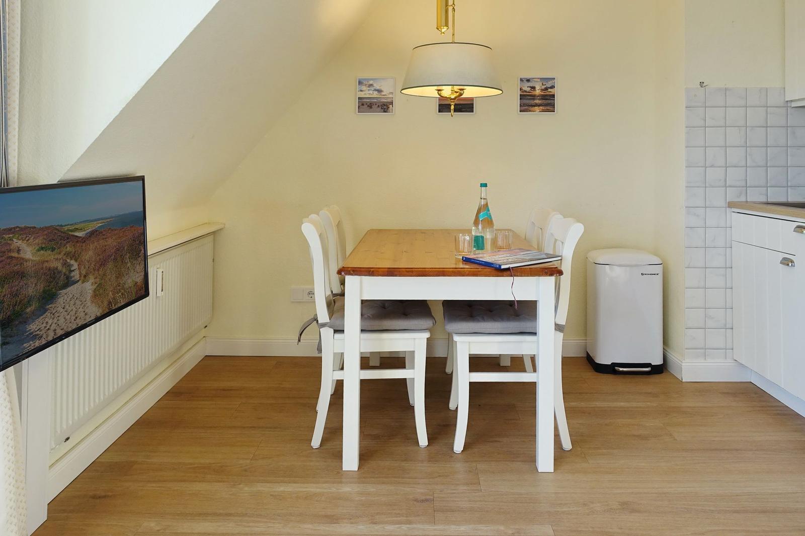 Dining area with table, chairs, and TV on the wall.