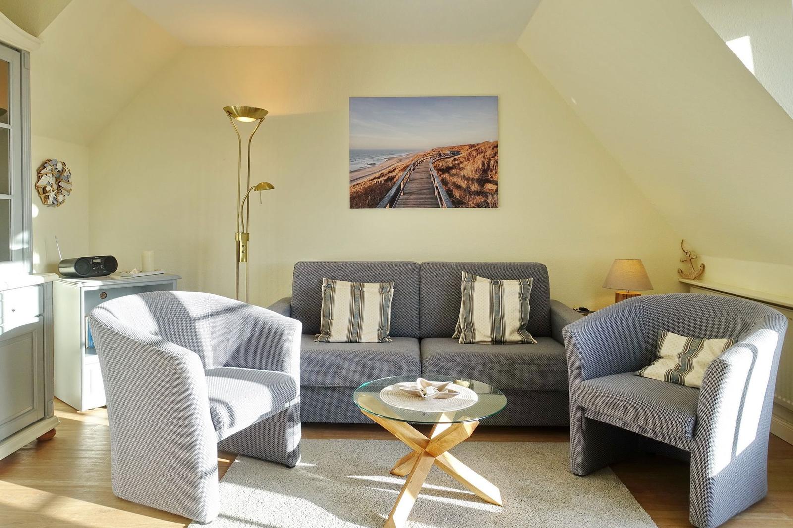Living room with sofa, two armchairs, and glass table under sloped ceiling.