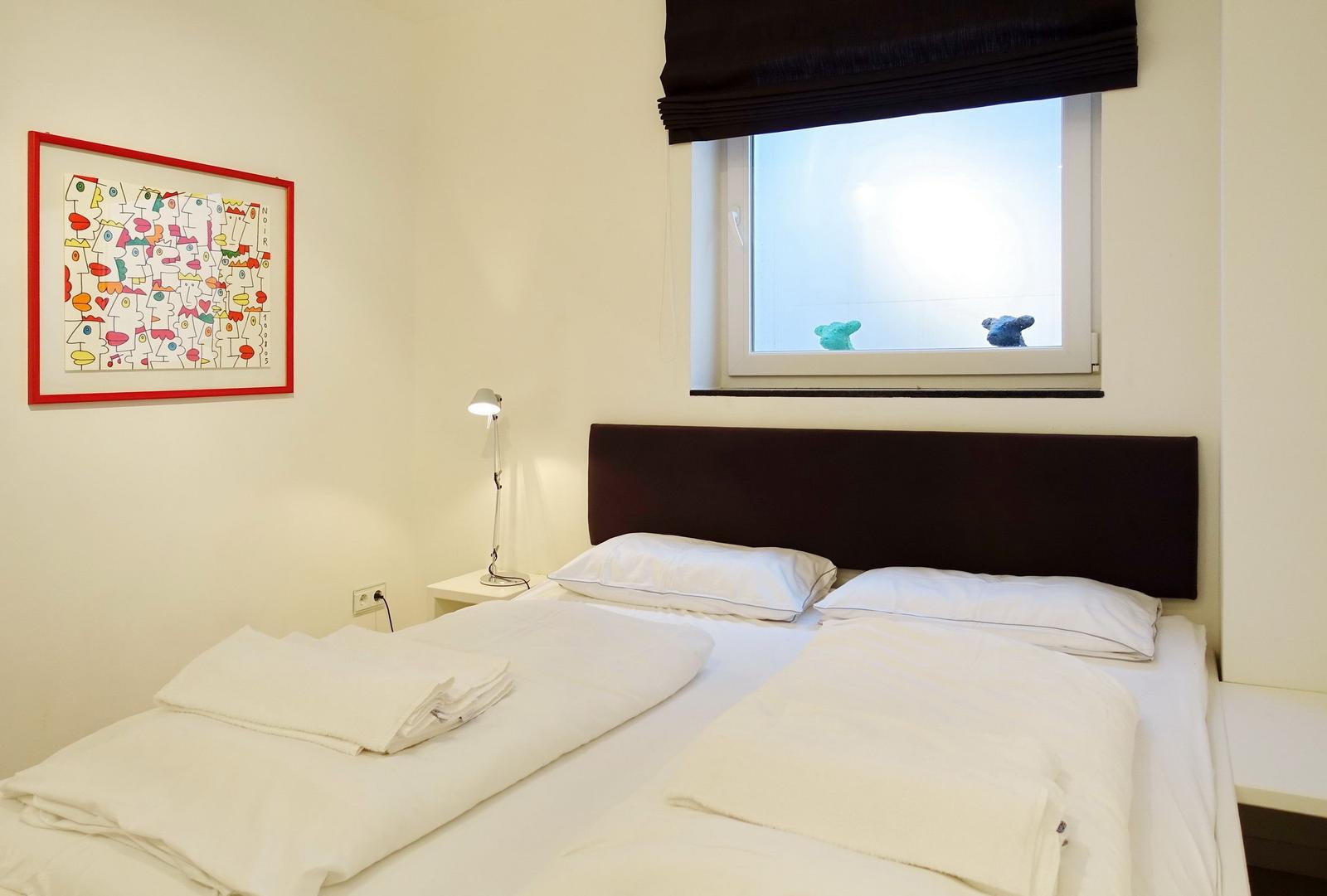 Bedroom with bed, nightstand, and window with artwork on the wall.