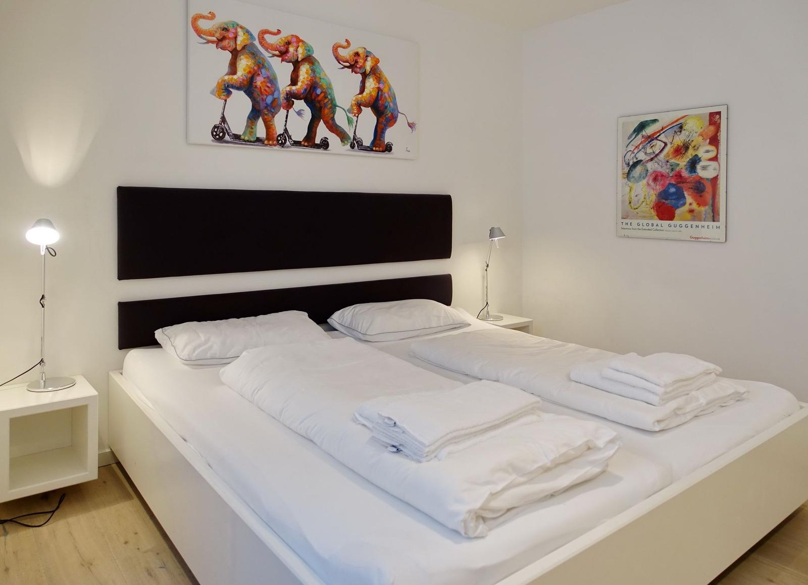 Bedroom with double bed, white linens, and wall art.