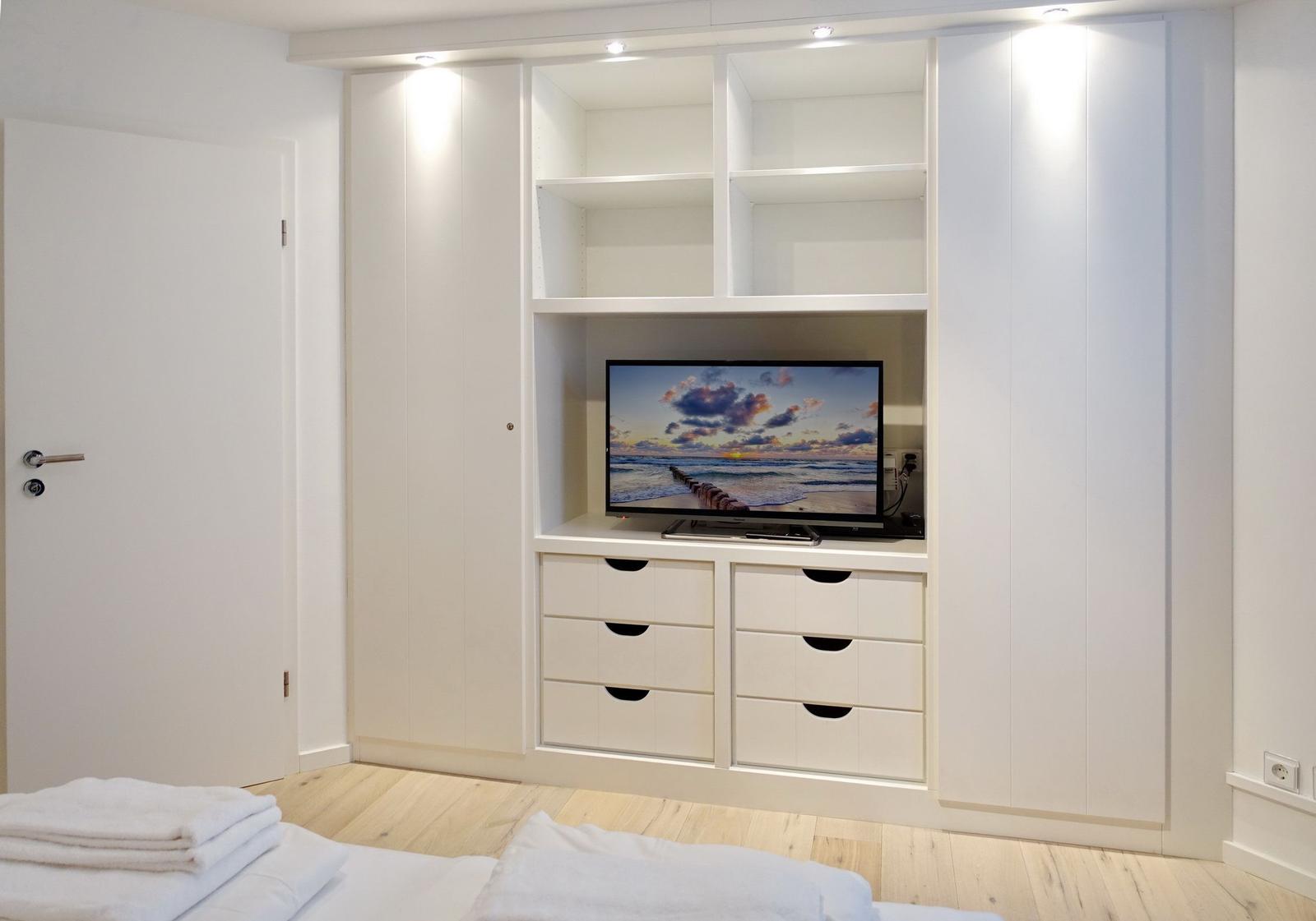Bedroom with white closet, TV, and wooden floor.