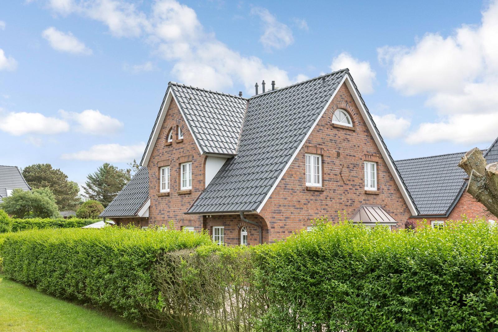 A two-story house with red brick walls and gray roof. Front garden with green hedge fence.