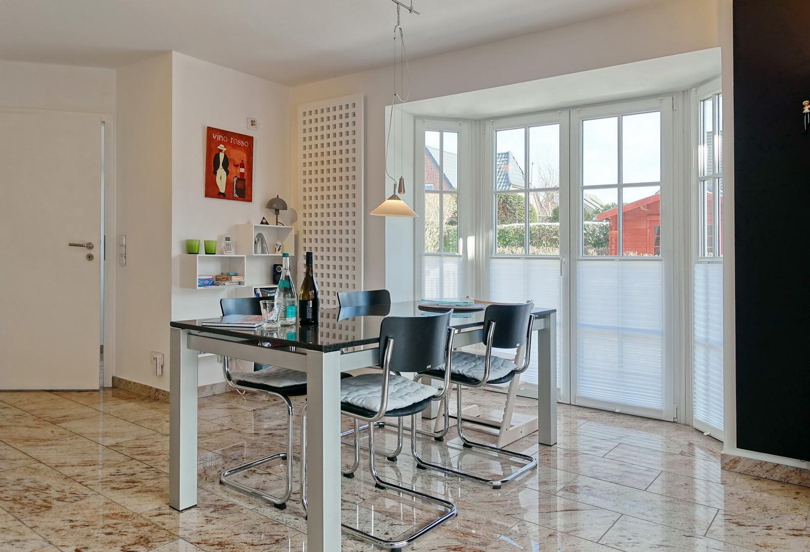 Dining area with table, chairs, and window front. Tile floor and wall shelf visible.