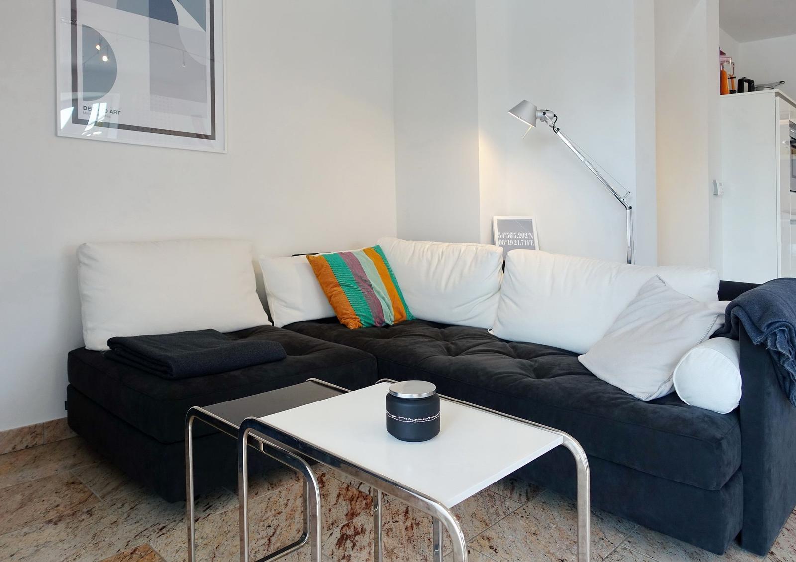 Black sofa with white cushions and colorful cushion. Table with candle and floor lamp.