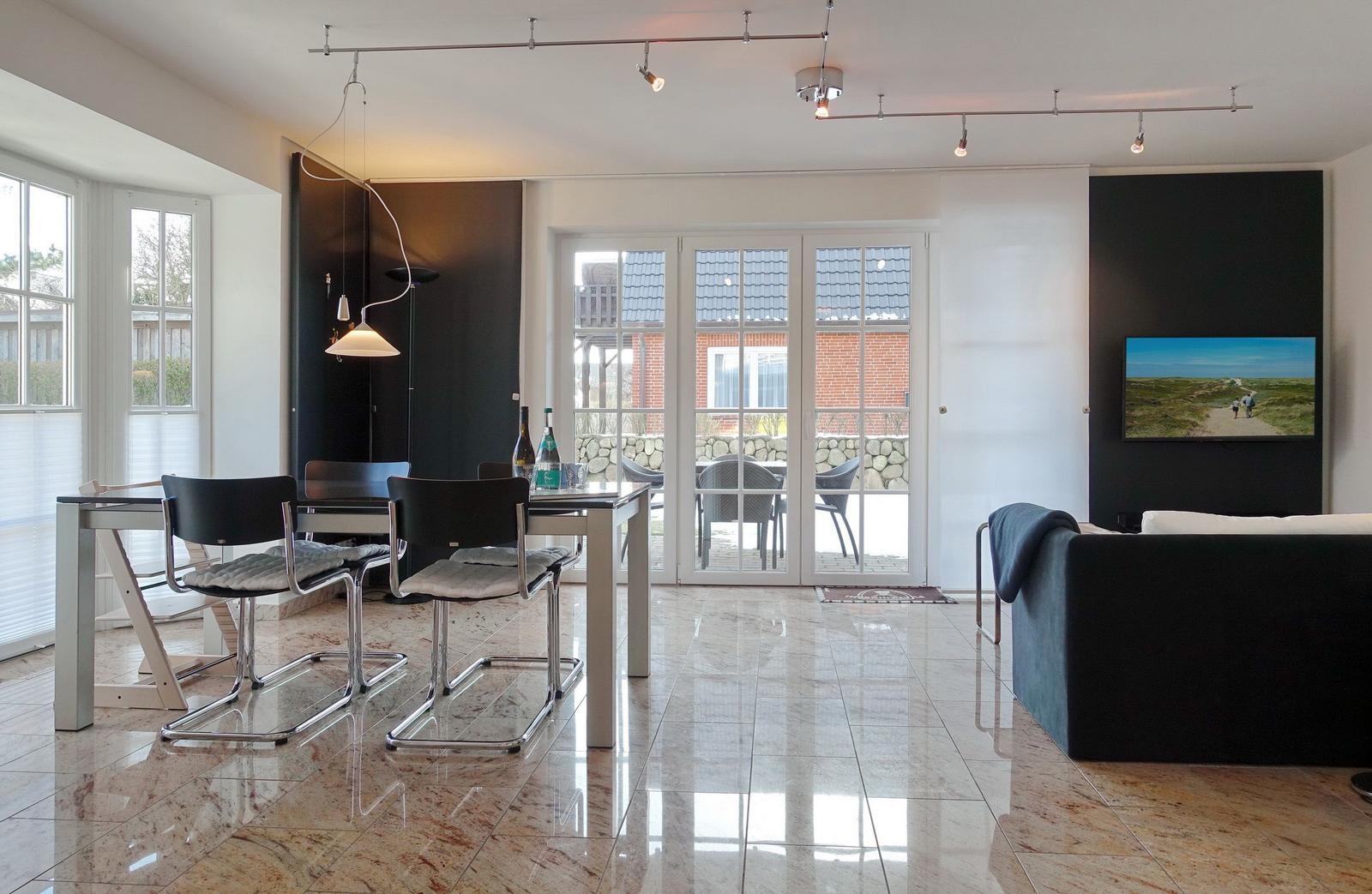 Modern furnished living area with dining table, sofa, and glass doors to the terrace.