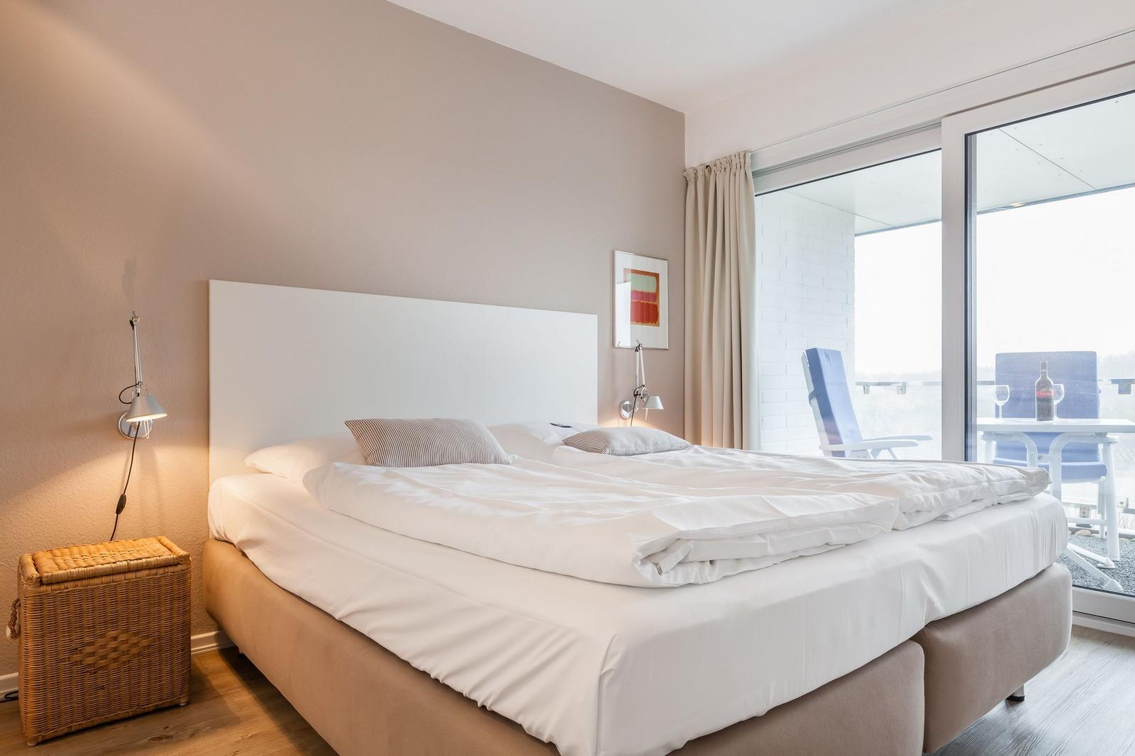 A bedroom with a double bed, desk, and balcony view.