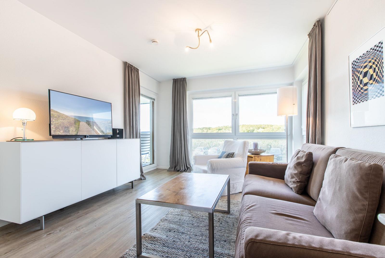 Living room with sofa, coffee table, and TV. View to balcony with landscape view.