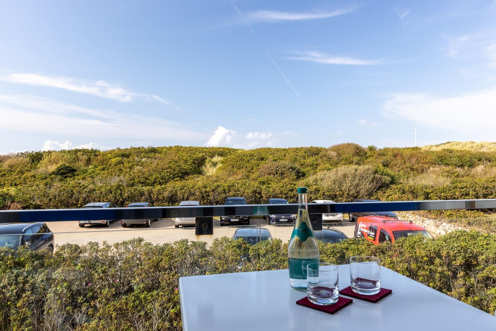 Table with bottle and glasses on balcony overlooking parking lot and green areas.