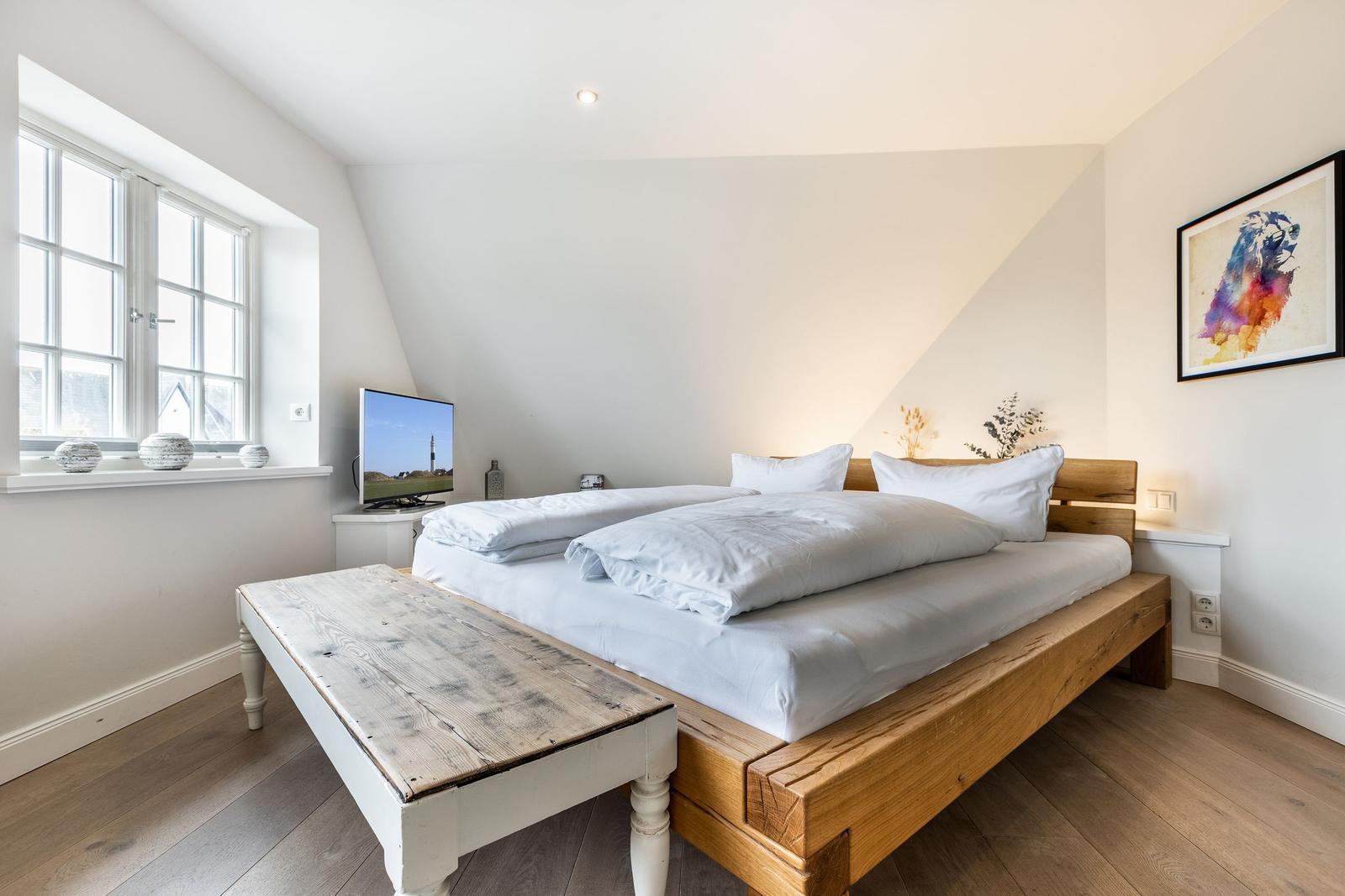 Bedroom with wooden bed, window, and TV.