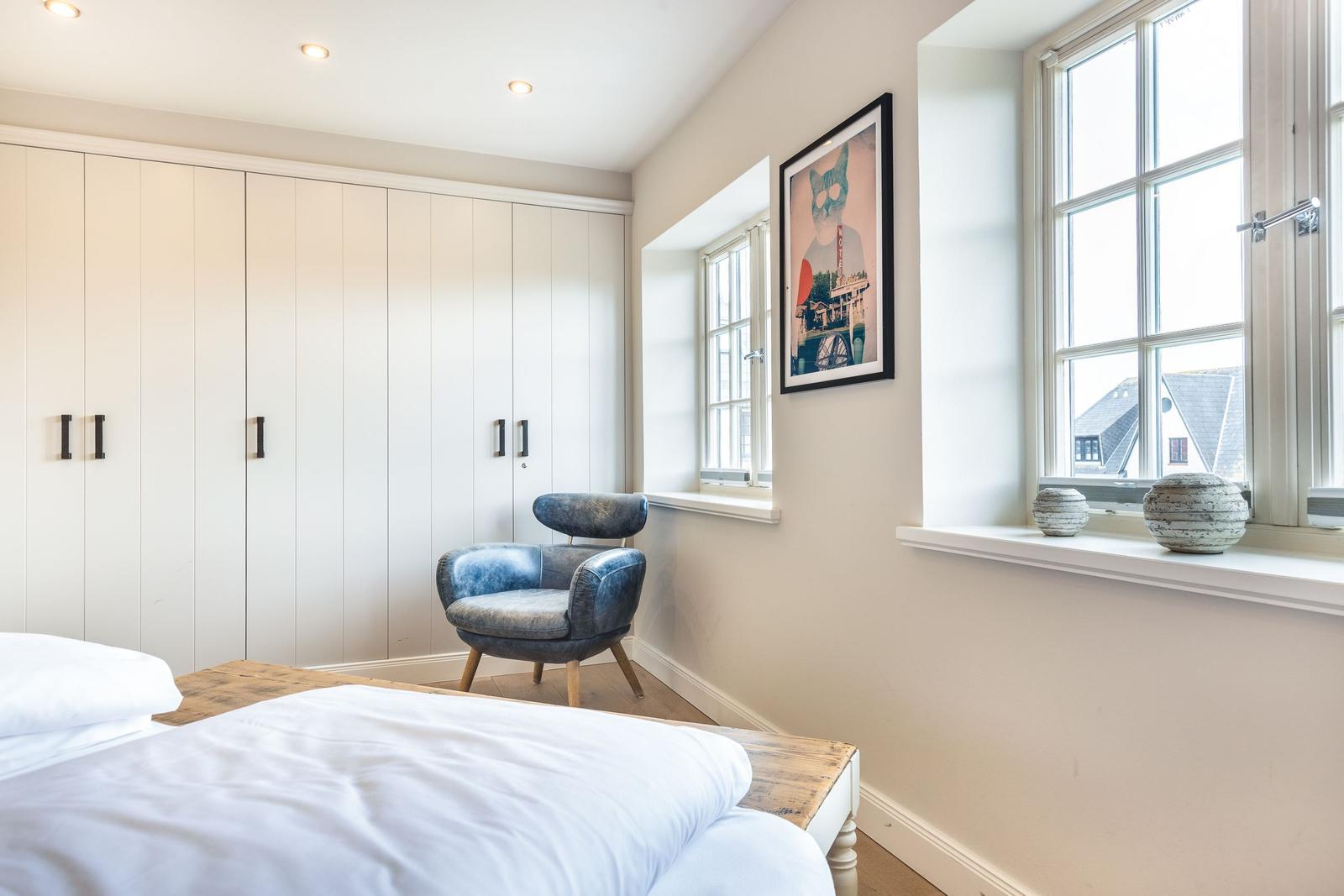 Bedroom with bed, wardrobe, and chair. Windows with view of outside area.