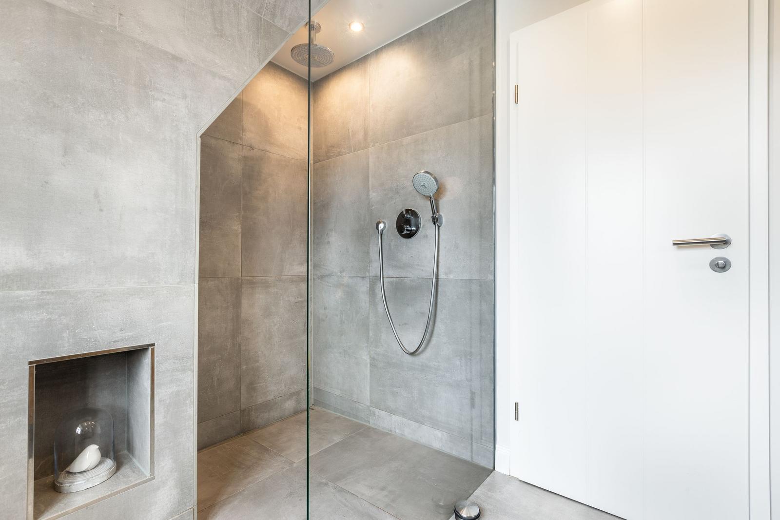 Shower cabin with glass wall and shower head. Niche with glass dome and white vase.