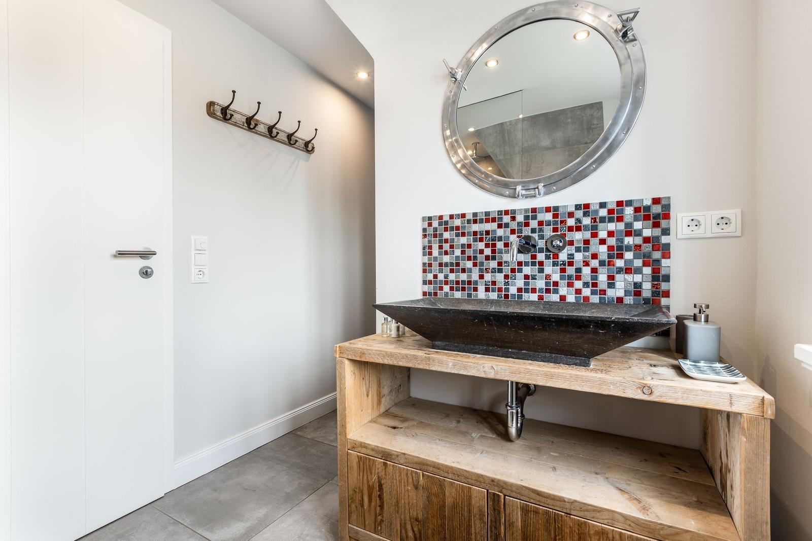 Bathroom with wooden vanity, mosaic wall, and round mirror.
