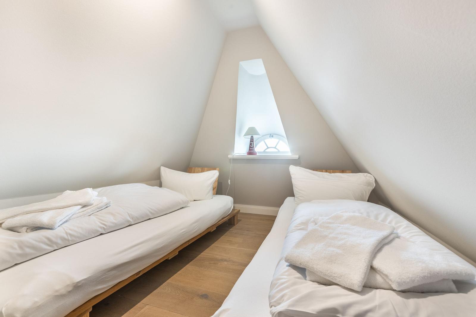 Two beds with white linens and towels under a skylight.