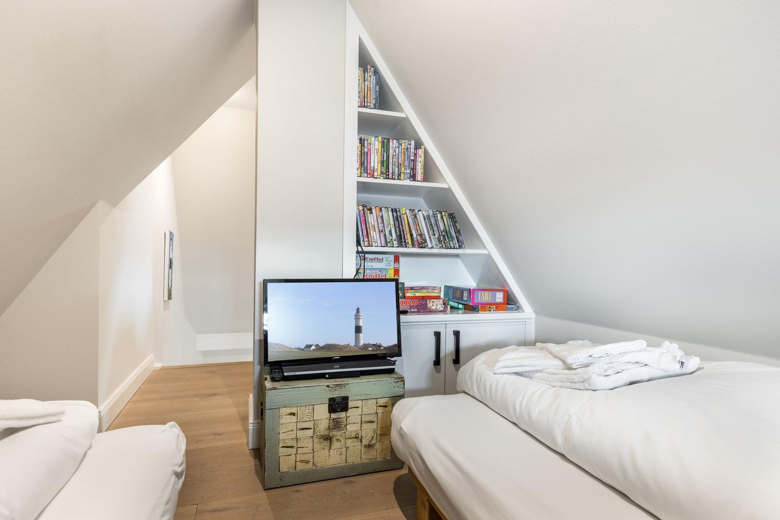 Room with double bed, TV, and bookcase under sloped ceiling.