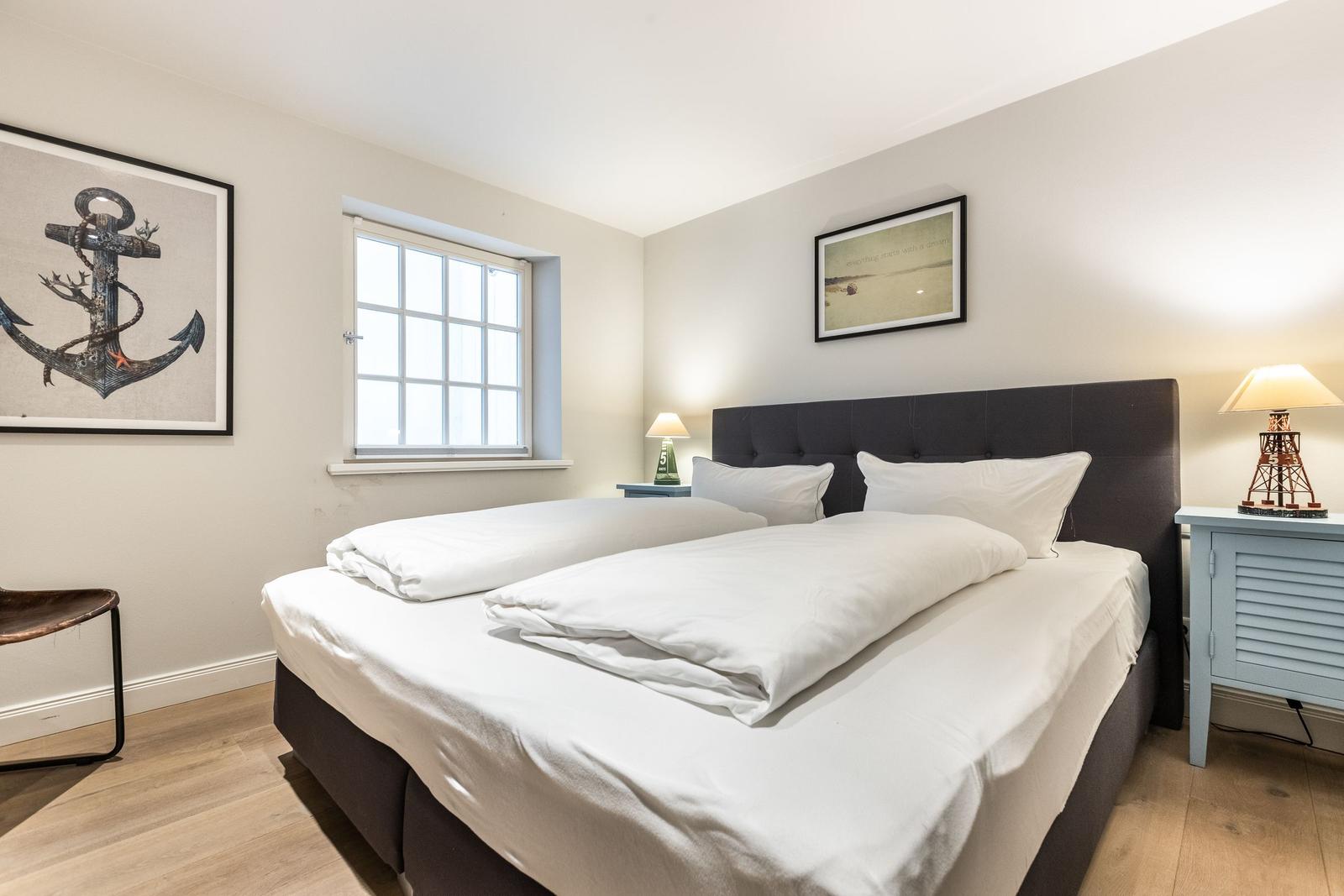 Bedroom with double bed, window, nightstands, and wall art.