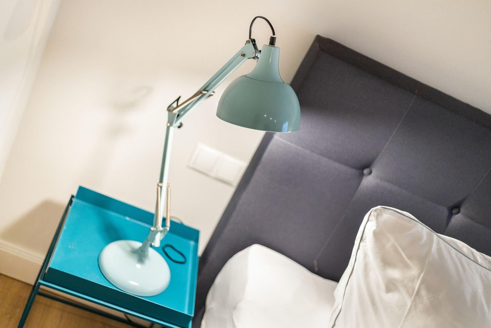 Bedroom with gray headboard, white bedding, and blue bedside lamp.